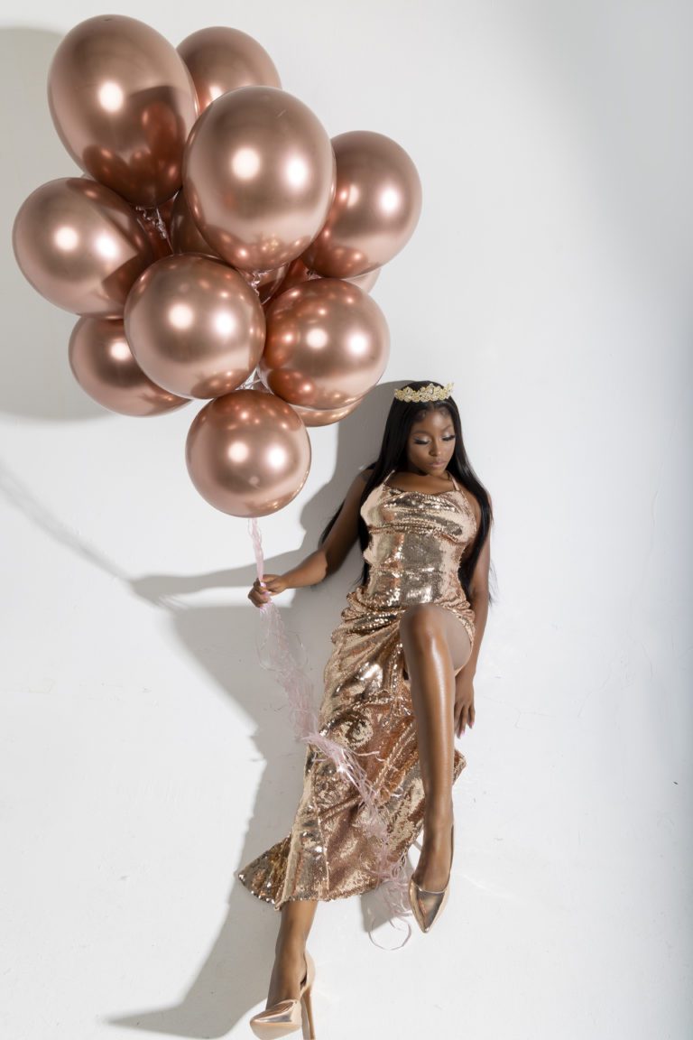 Woman in bronze dress holding a bunch of bronze balloons