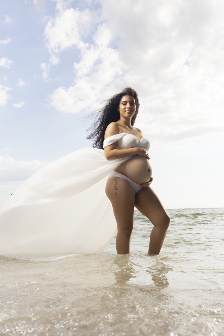 Pregnant woman in white standing on shore