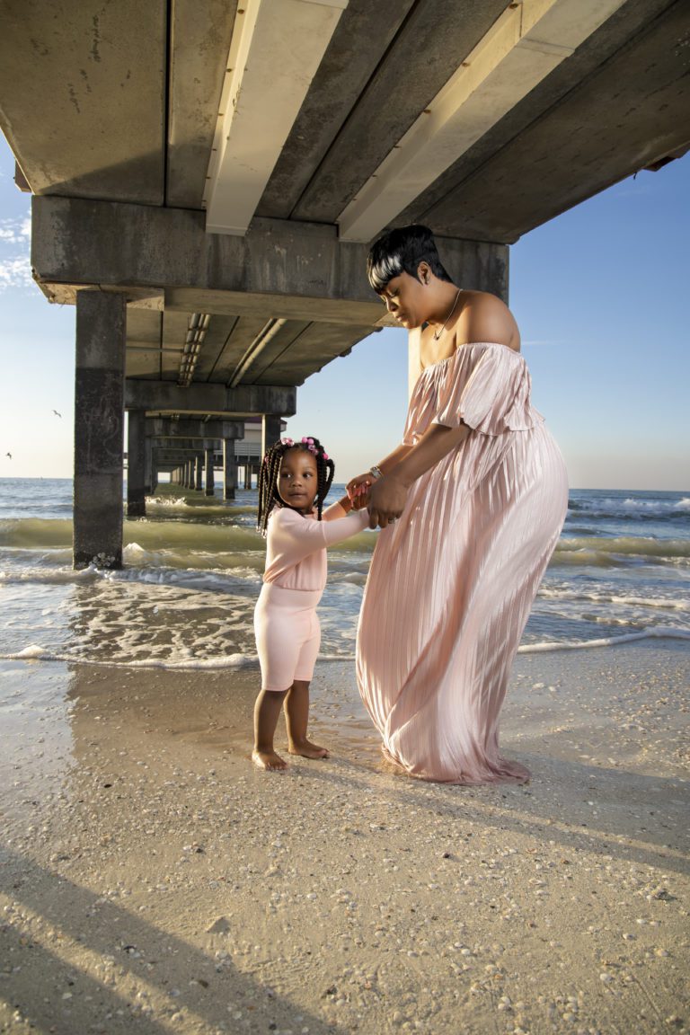 Mother and young daughter on shore under boardwalk